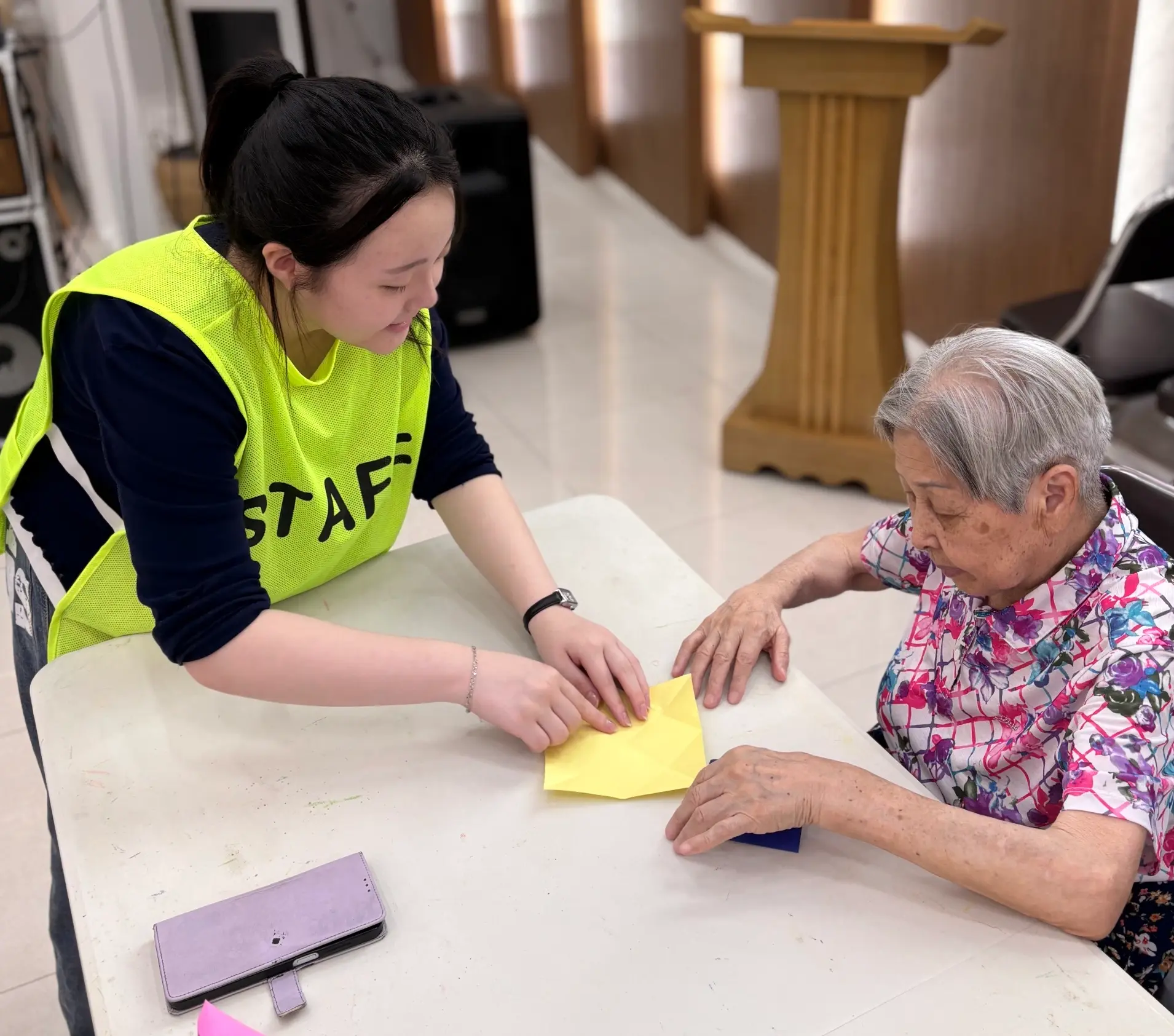 Chaeyoon folding origami with an elderly woman at the senior center