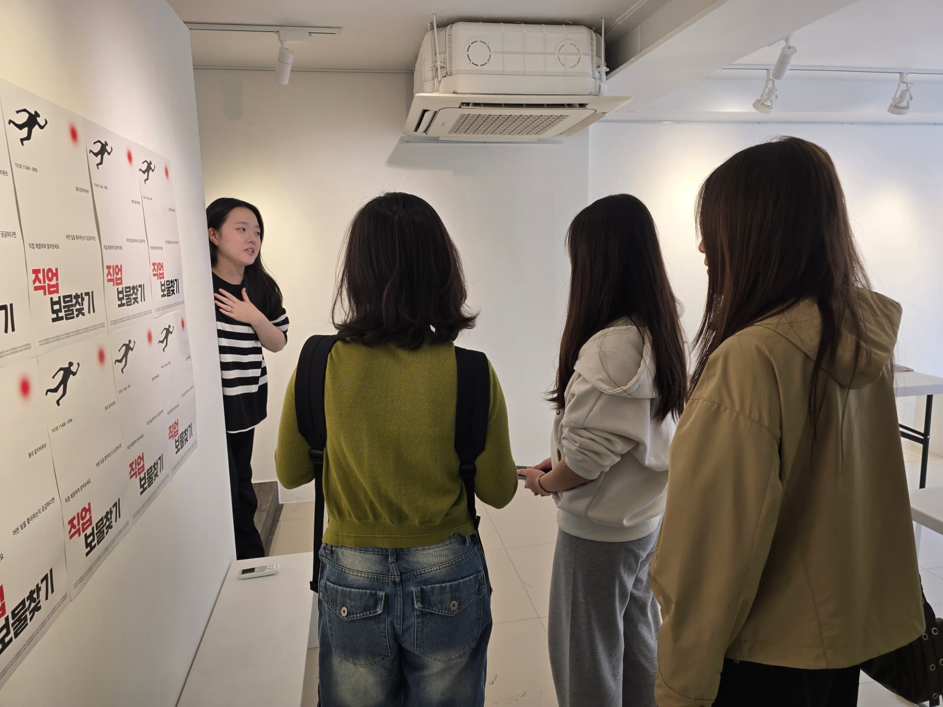 Talking with a group of students in a gallery beside a wall of career treasure-hunt posters