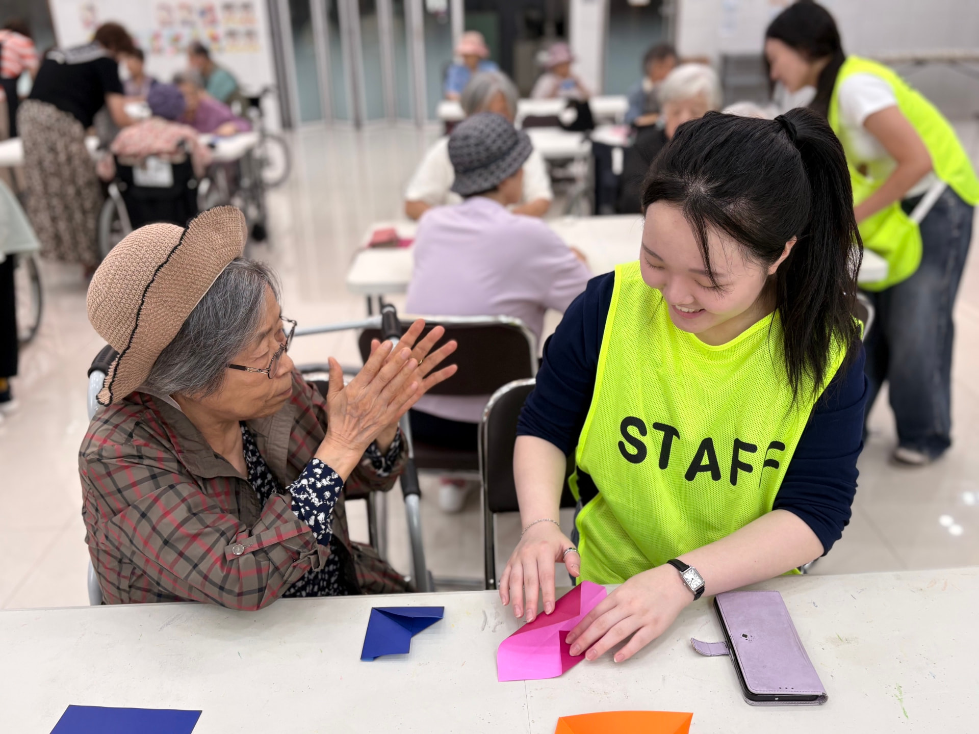 Chaeyoon folding paper with a smiling senior who claps along