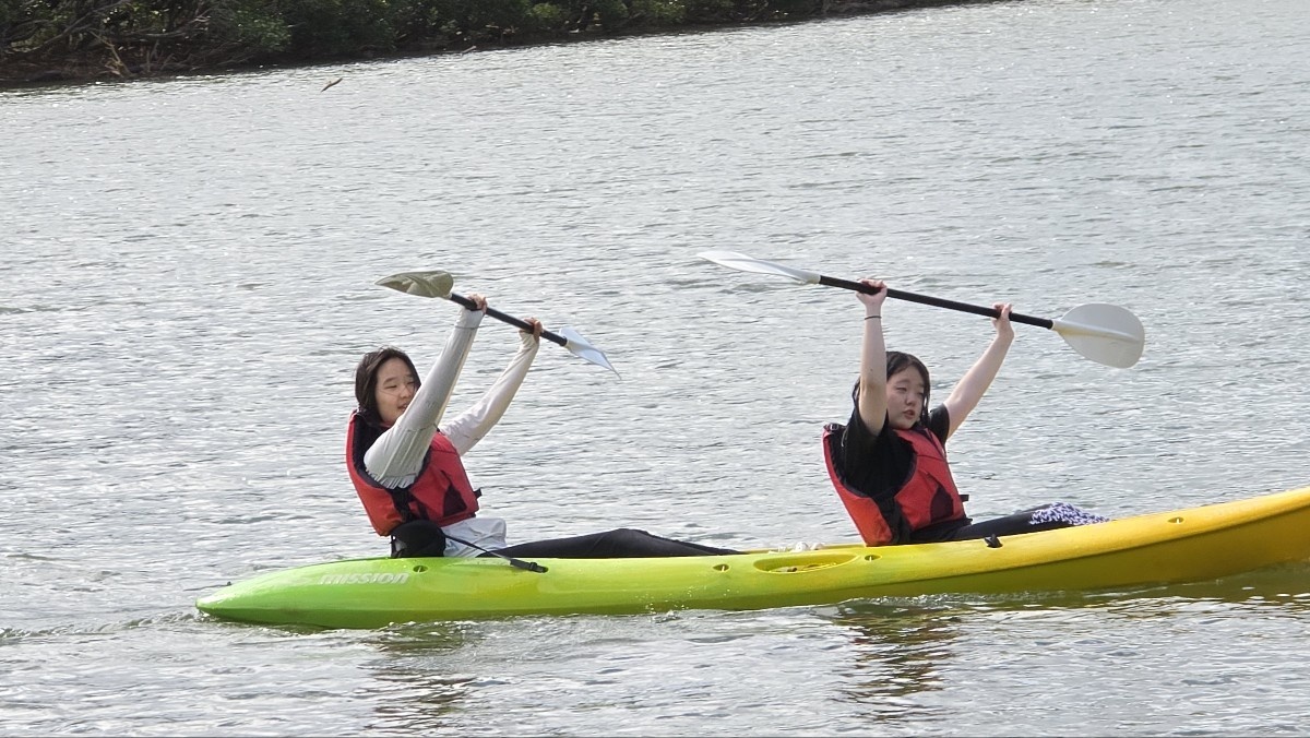 Chaeyoon and a friend raising their paddles in a kayak